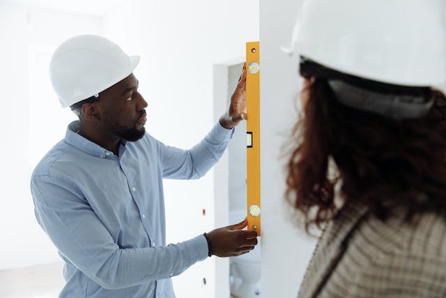 two-people-in-hardhats-using-a-level-to-measure-a-wall two-people-in-hardhats-using-a-level-to-measure-a-wall